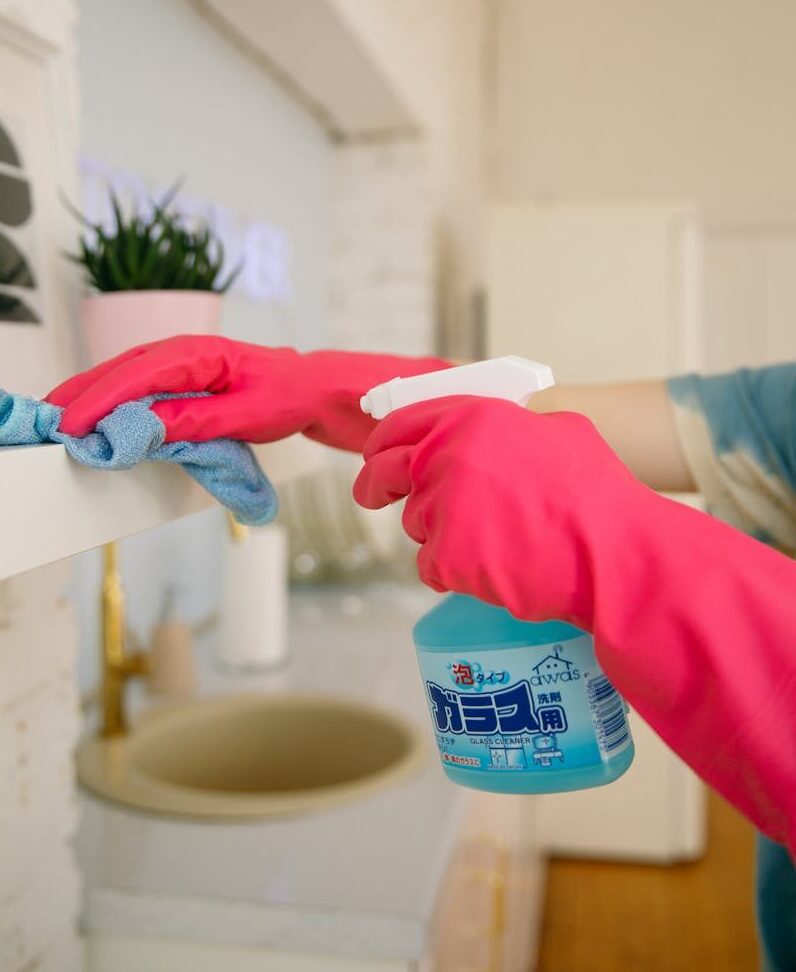 Person using spray bottle and cloth for cleaning a kitchen shelf, ensuring hygiene and cleanliness.